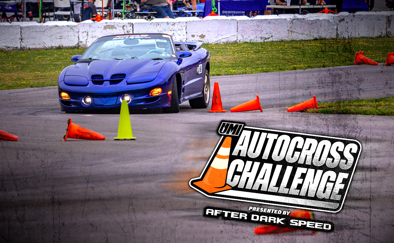 A blue sports car navigates an autocross course marked by orange cones, with a large "Autocross Challenge" logo overlayed in the foreground.