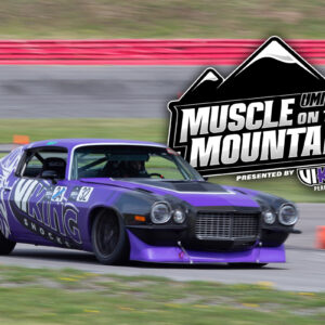 A purple race car speeds on a track with the "Muscle on the Mountain" event logo in the background.