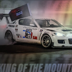 A white car with the number 59 and sponsor decals drifting on a racetrack, producing smoke. The text "2024 King of the Mountain" is partially visible at the bottom.