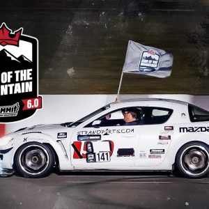 A white car with a flag on it is driving down a race track.