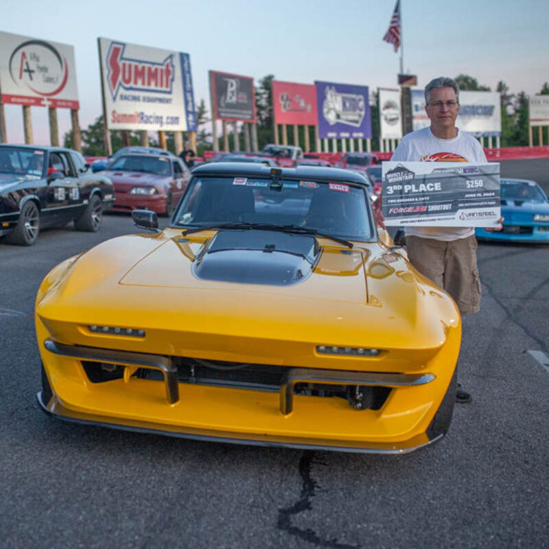 A man stands beside a yellow sports car holding a "3rd Place" award. Other cars and signage are visible in the background.