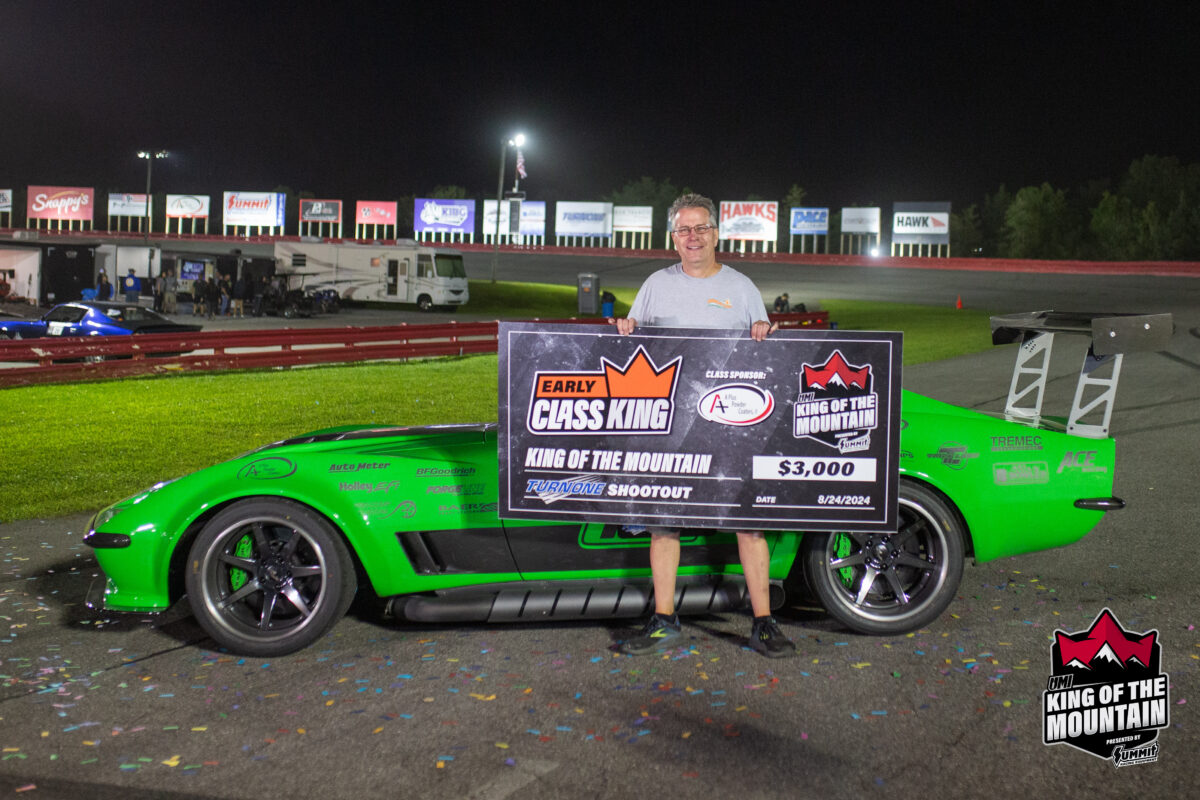 A person standing on a racetrack holds a large check for $3,000 and a sign reading "Early Class King" next to a bright green race car. The event is labeled "King of the Mountain.