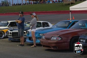 A group of people standing next to a row of cars.