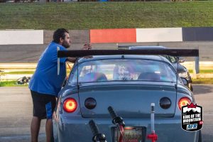 A man standing next to a car at a race track.