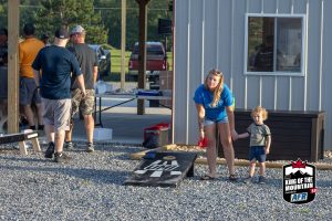 A group of people playing cornhole in a gravel area.