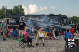 A group of people sitting around a campfire in front of an rv.