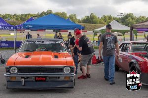 A group of people standing next to an orange car at a car show.
