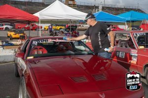 A man standing next to a red car at a race.