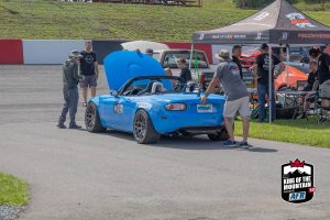 A blue mazda mx-5 parked next to a tent.