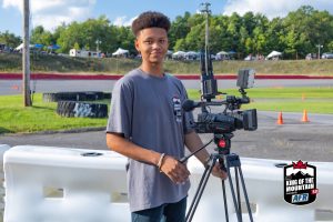 A young man with a camera standing next to a fence.